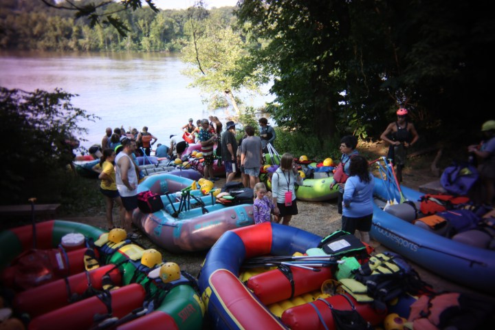 Group of people preparing for rafting by the river, surrounded by colorful inflatables and equipment.