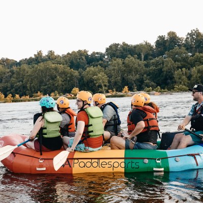 Group of people wearing helmets and life vests rafting on a river.