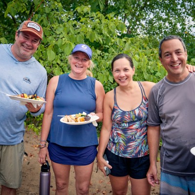Four people smiling, standing outdoors and holding plates with food.