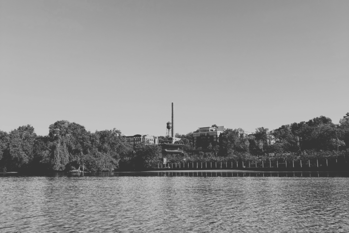Black and white photo of a lake with trees and a tall structure in the background.